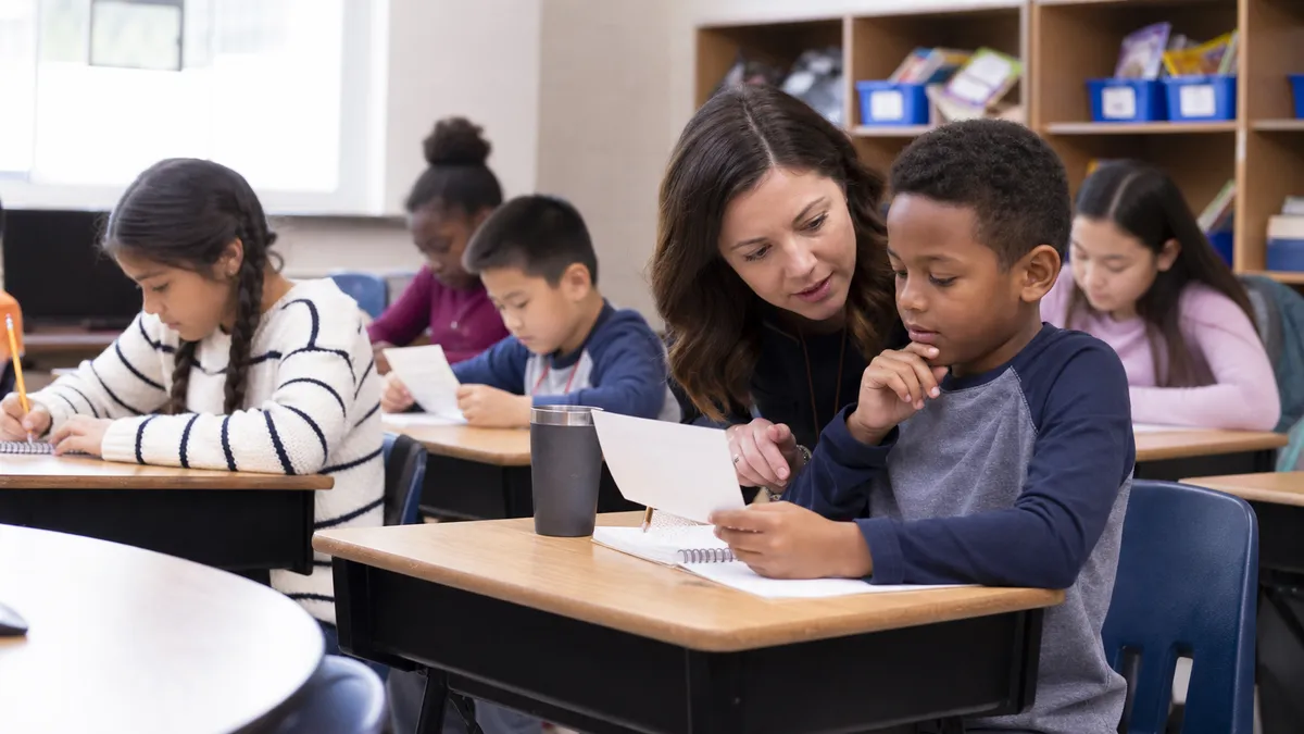A U.S. elementary teacher helps a student compare a source page with a newly written notebook sentence.